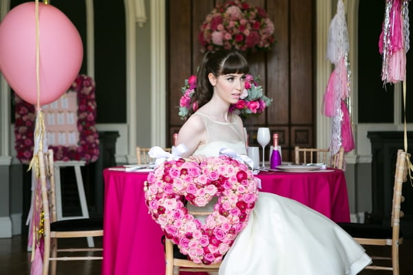 Bride sitting on chair with pink floral heart