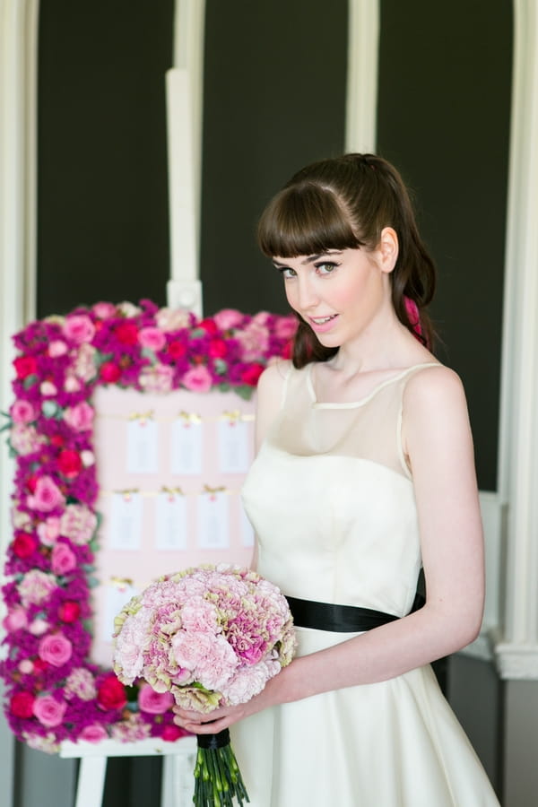 Bride standing next to pink floral table plan