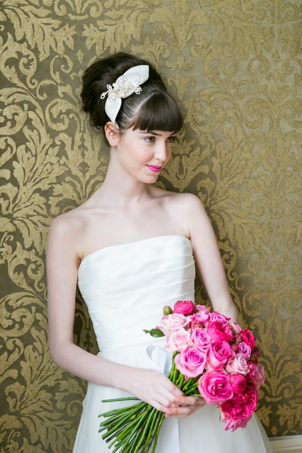 Bride leaning against wall holding pink bouquet