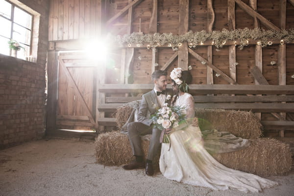 Bride and groom sitting on hay bale in barn