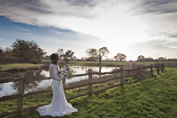 Bride leaning on fence in countryside
