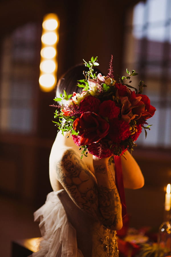 Bride hiding face with red bouquet