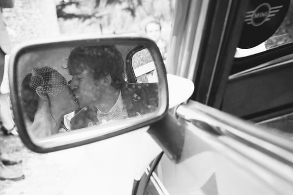 Reflection of bride and groom kissing in car wing mirror