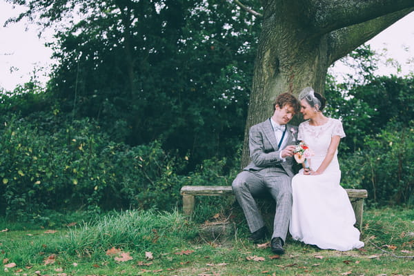 Bride and groom sitting on bench by tree
