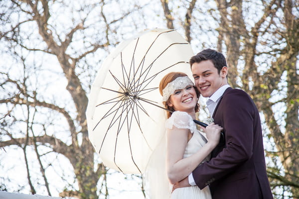 Bride and groom holding parasol and smiling