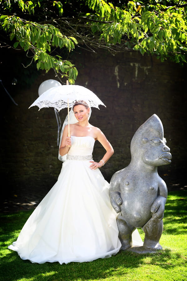 Bride with parasol standing next to statue in Walton Castle grounds