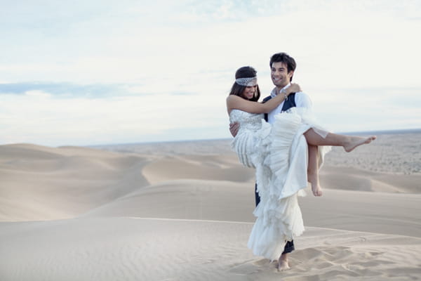 Groom carrying bride across desert