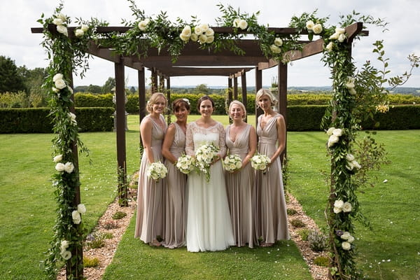 Bride and bridesmaids standing under floral canopy by Louise Avery Flowers