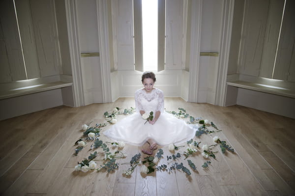 Bride sitting on floor surrounded by roses