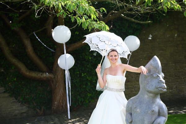 Bride holding parasol leaning on statue