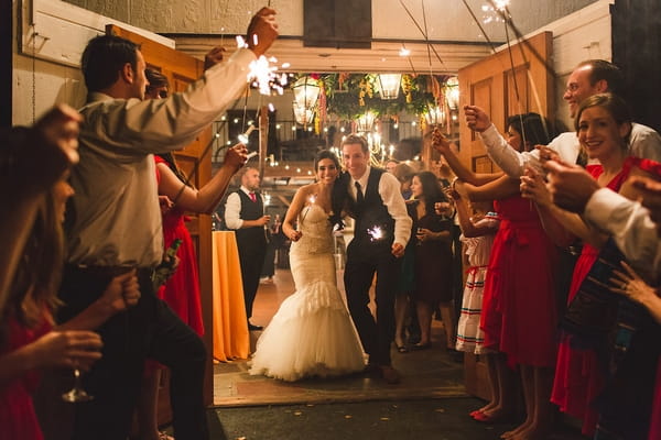 Bride and groom leaving reception with guests holding sparklers