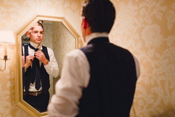 Groom doing up tie in mirror