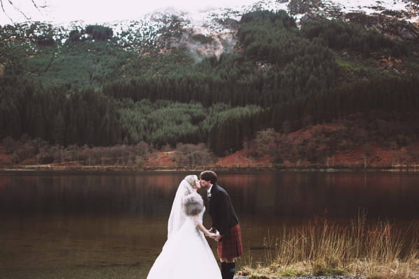 Bride and groom kissing in front of loch