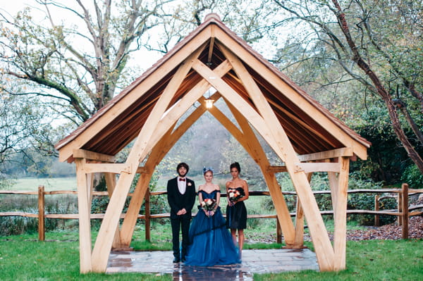 Bride, groom and bridesmaid under wooden frame