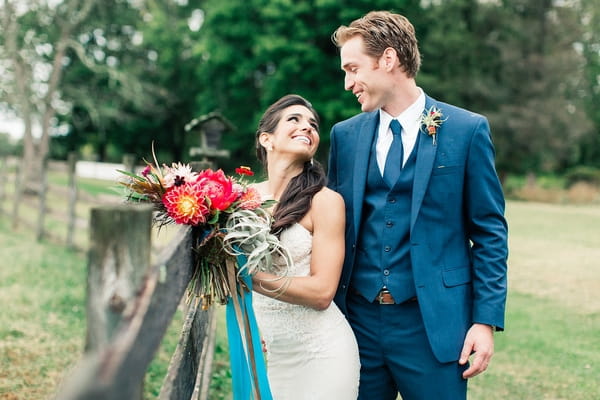 Bride and groom leaning on fence on farm