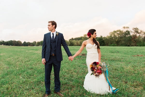 Bride and groom holding hands looking away from each other