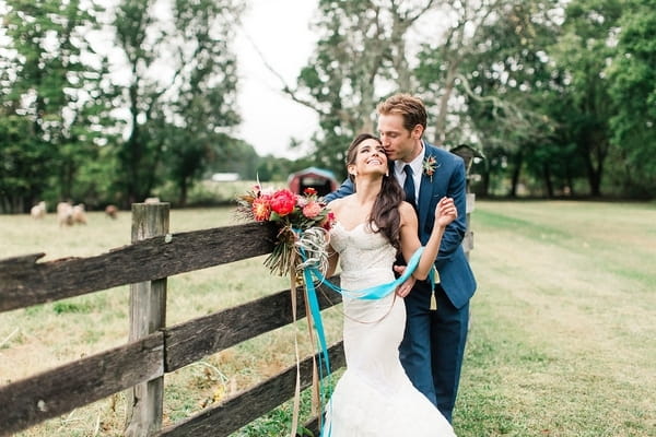 Bride and groom by fence on farm