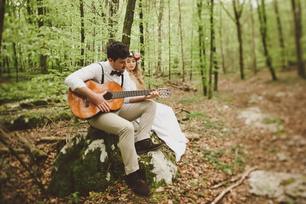 Groom playing guitar to bride in woods