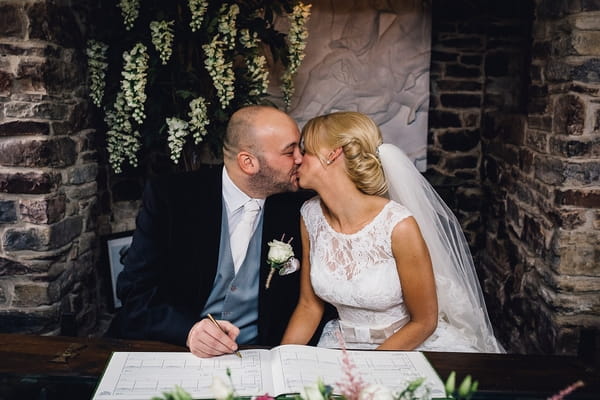 Bride and groom kiss while signing register