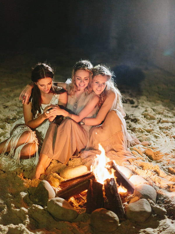 Bohemian bridesmaids sitting by fire on beach