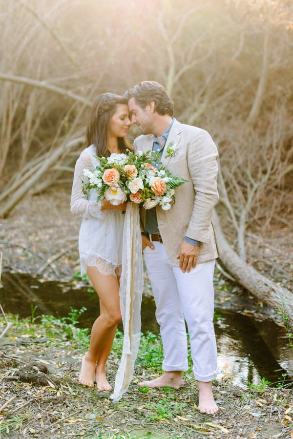 Bride and groom touching heads next to creek