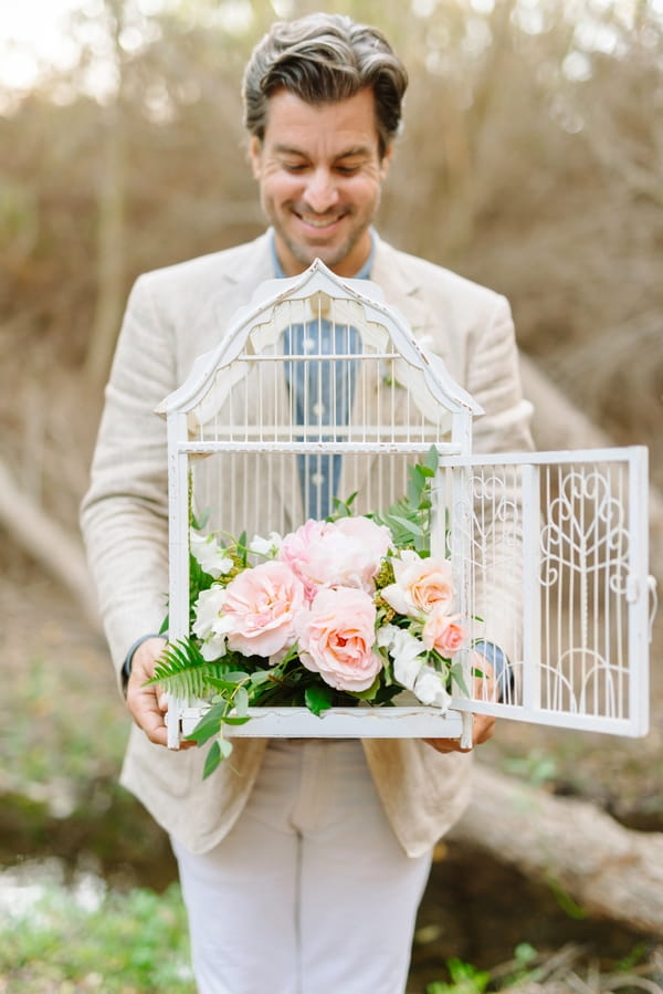 Groom holding birdcage with flowers in