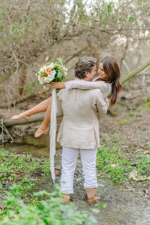 Groom carrying bride in creek