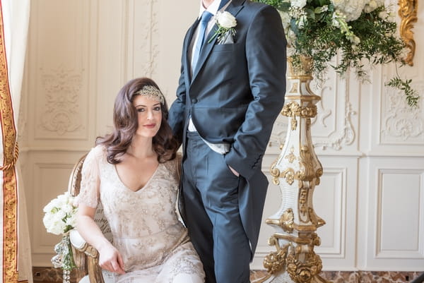 Bride sitting in chair with groom standing