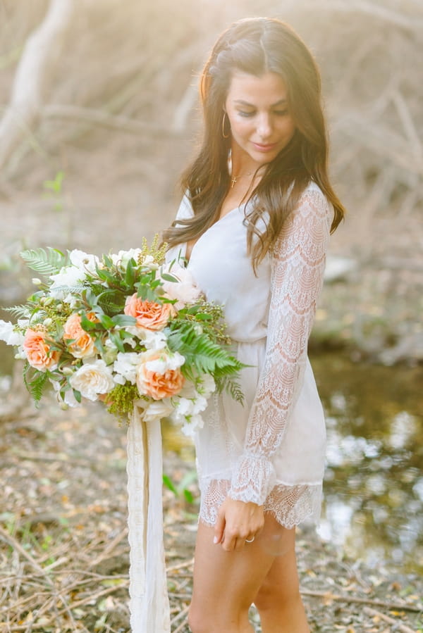 Bride with lace detailed sleeved top holding bouquet