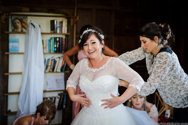 Bride smiling while putting wedding dress on