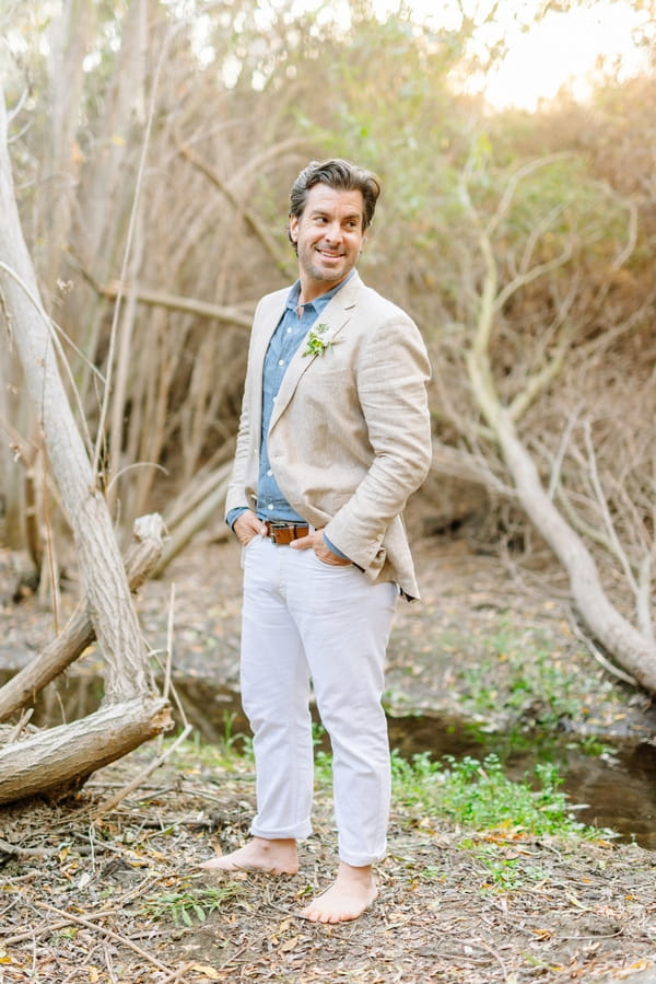 Groom with hands in pockets standing by creek