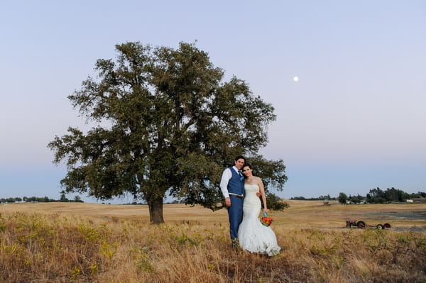 Bride and groom in field by tree