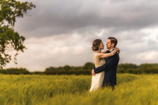 Bride and groom with arms around each other in field - Picture by Andrew Keher Photography