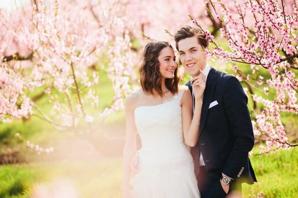 Bride and groom standing amongst blossom covered trees