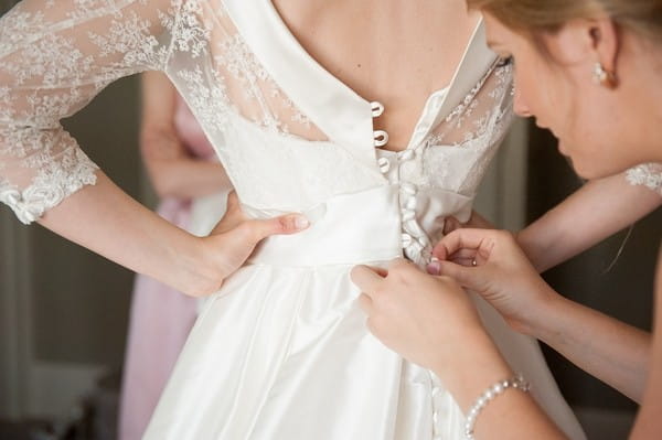 Doing up buttons on back of bride's dress