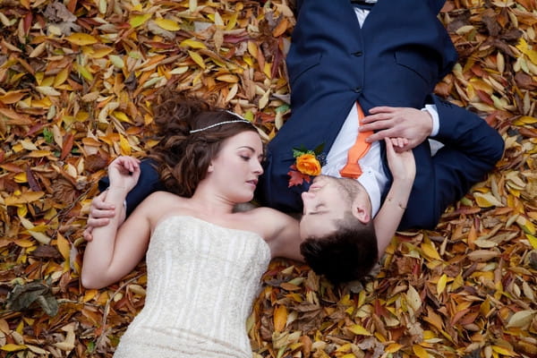 Bride and groom laying in autumn leaves