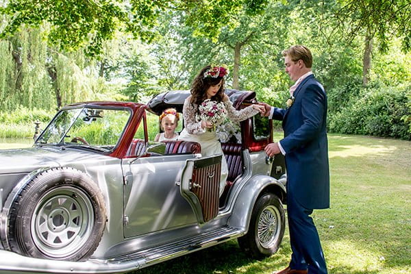 Groom helping bride out of wedding car
