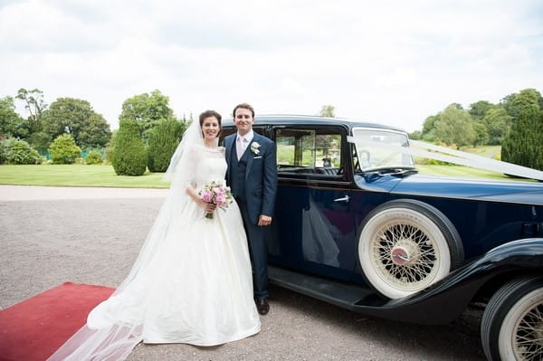 Bride and groom standing by wedding car