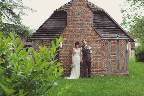 Bride and groom standing by wall of Chilham Village Hall in Kent