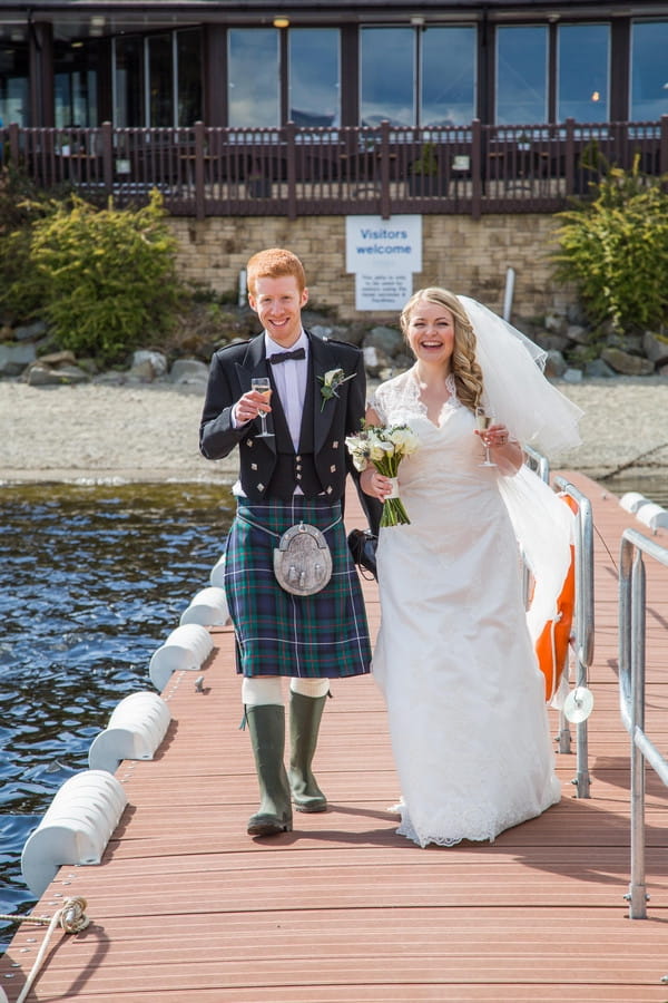 Bride and groom walk down jetty at Loch Lomond
