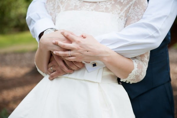 Bride holding grooms hands around waist