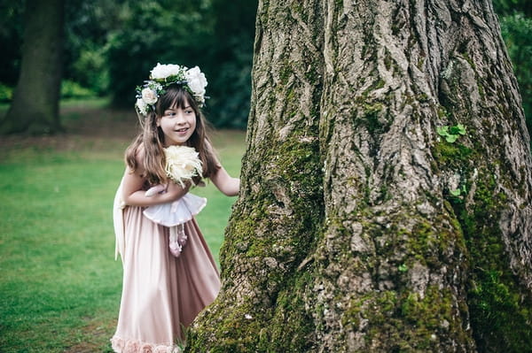 Young flower girl peeking out from behind tree