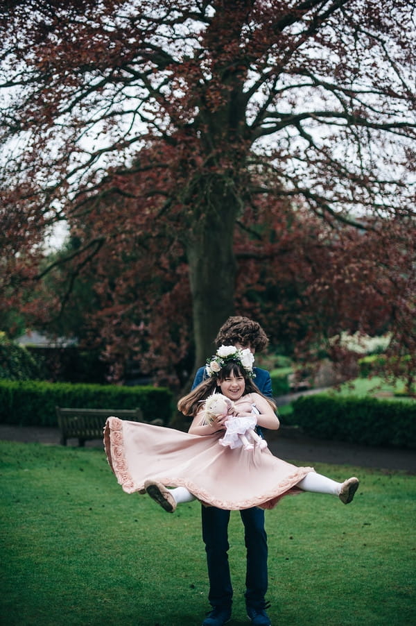 Young groomsman lifting up flower girl