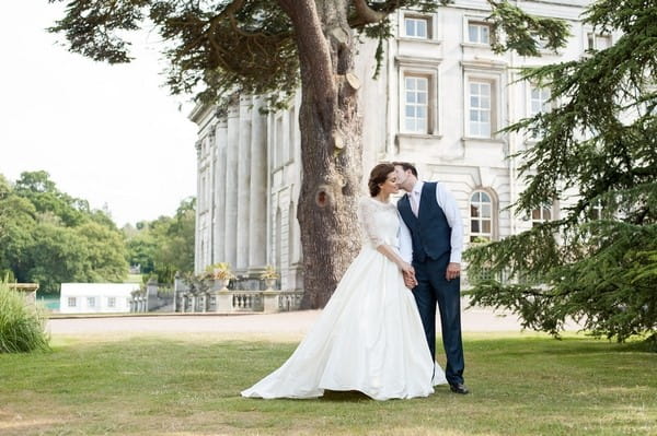Groom kissing bride on cheek outside Moor Park Mansion