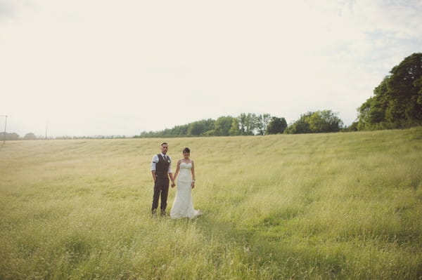 Bride and groom holding hands in field