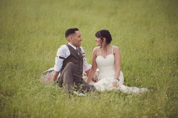 Bride and groom sitting on grass in field
