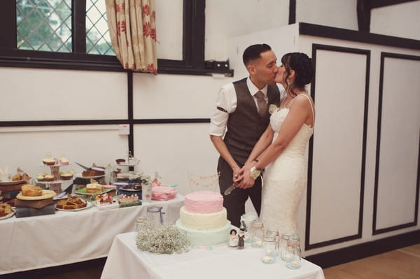 Bride and groom kiss as they cut the cake