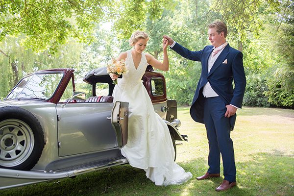 Groom helping bride out of vintage wedding car