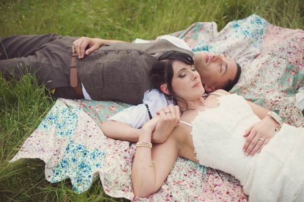 Bride and groom laying on rug on grass