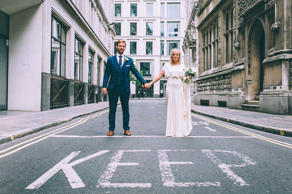 Bride and groom holding hands behind word KEEP written on road in London